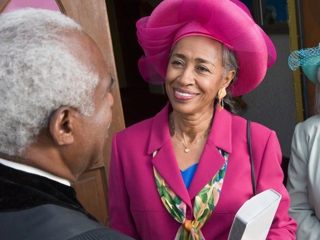 Photo of an older African-American woman in a pink suit speaking to an African-American pastor about COVID-19 symptoms.