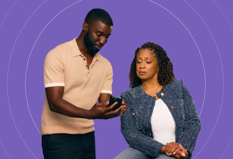 Photo of a young African-American man sharing information on his phone to an older woman with COVID-19 high risk factors.