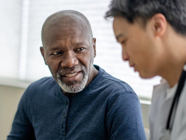 Photo of an older African-American man speaking to a young Asian man in a grey shirt about COVID-19 signs and symptoms.