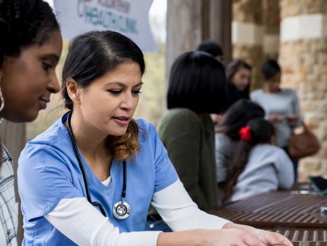 Photo of a young Latina nurse speaking to a young African-American woman about the COVID-19 impact on the Black community.