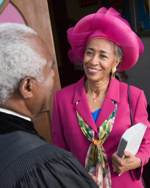 Photo of an older African-American woman in a pink suit speaking to an African-American pastor about COVID-19 symptoms.
