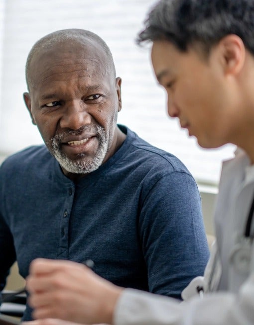 Photo of an older African-American man speaking to a young Asian man in a grey shirt about COVID-19 signs and symptoms.