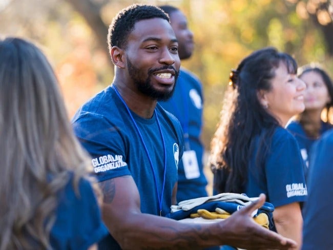 Photo of volunteers sharing COVID-19 signs and symptoms. A young African-American man offers a handshake in the foreground.