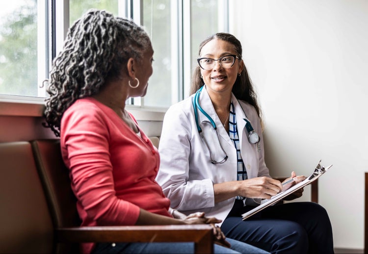 Photo of a young African-American doctor discussing COVID-19 signs and symptoms with an older African-American woman.