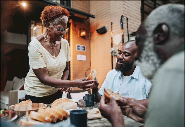 Photo of a older African-American woman with COVID-19 high risk factors sharing food with family at the dinner table.